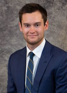 Portrait of Tyler Tumey in blue suit with gray background