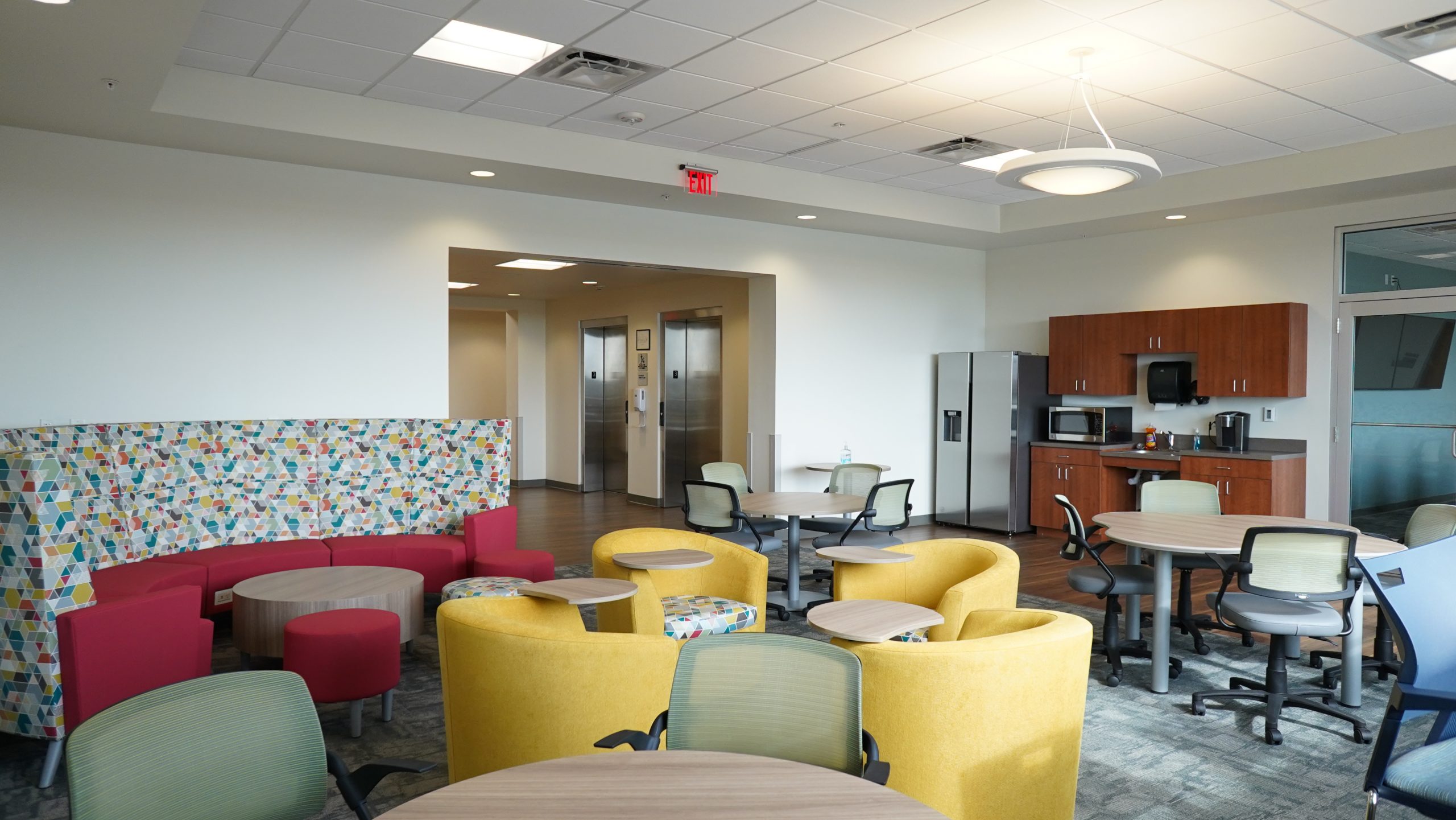 Student lounge with yellow chairs and kitchen area.