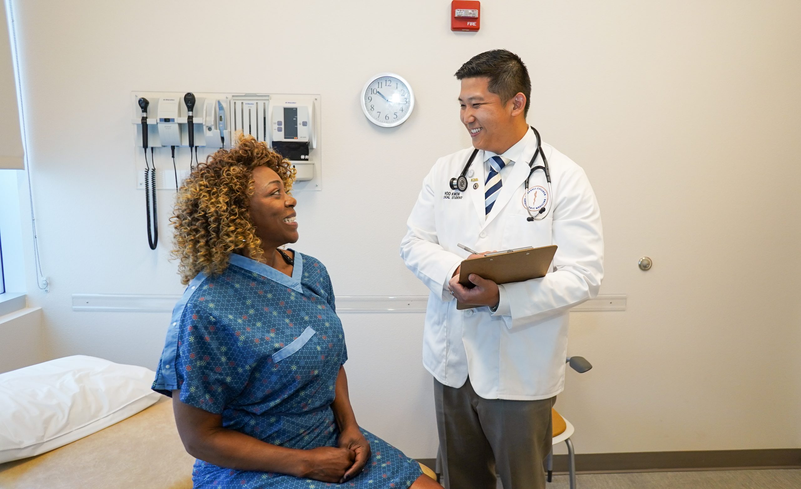 A medical student smiles at a patient in an exam room.