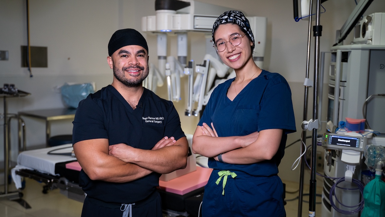 Two medical students standing in front of an operating room, smiling with their arms folded.