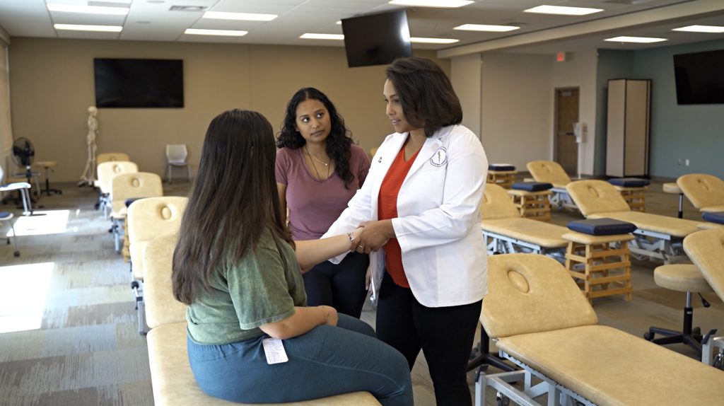 Three students practicing assessing a patient in a classroom